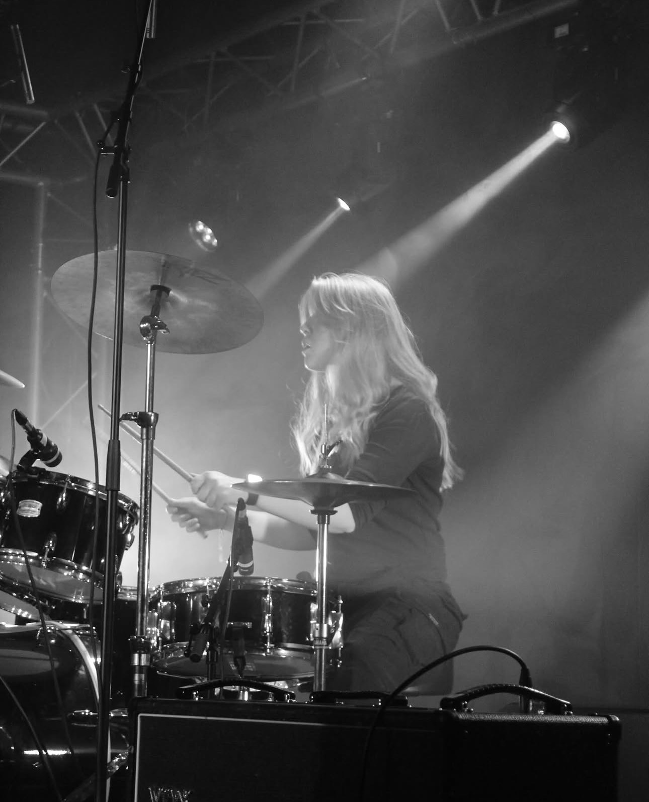 Aeryn behind the drum kit under stage lights, mid-performance
