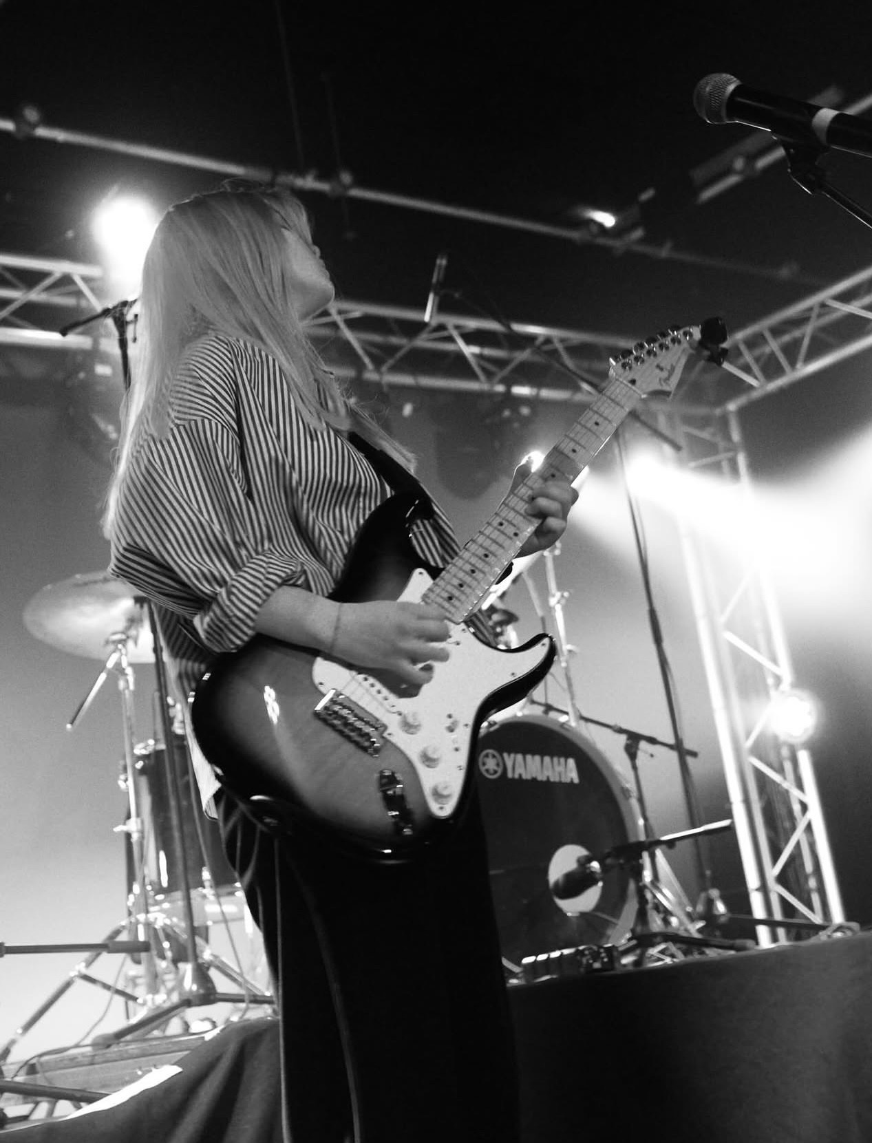 Aeryn playing electric guitar on stage, backlit by stage lights