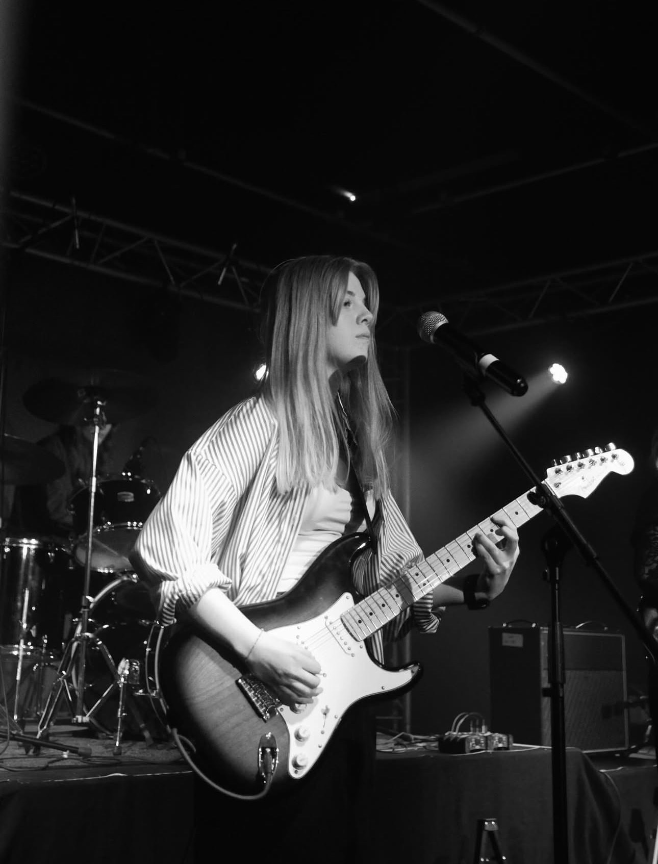 Aeryn singing into a microphone while playing electric guitar